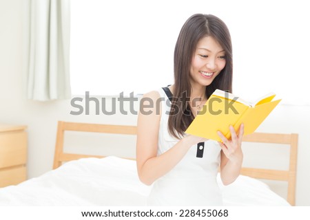 young attractive asian woman who reads a book in bed
