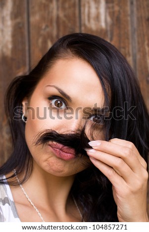 A glamour close-up of a funny young brunette placing her hair under her nose as if mimicking a moustache