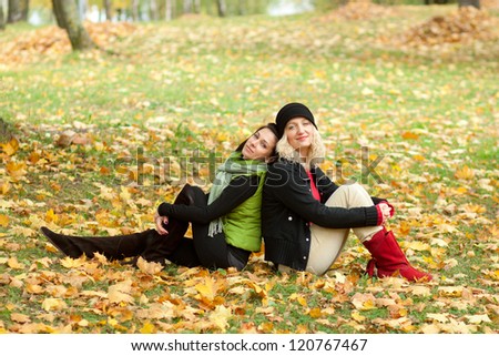 Two young women sitting back to back in autumn park