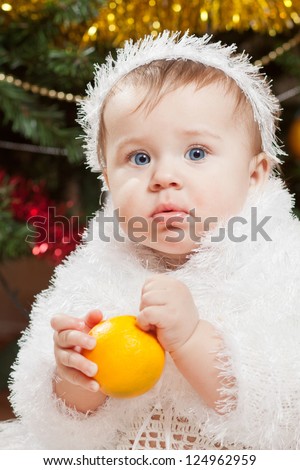 Happy little baby girl playing with fruits under the christmas tree