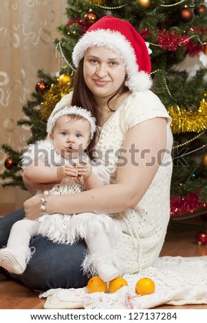 Happy little baby with her mother sitting under the christmas tree