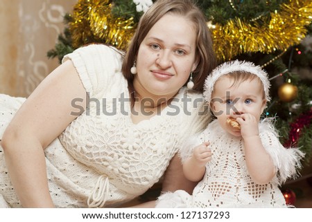 Happy little baby with her mother sitting under the christmas tree