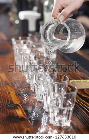 Bartender pouring glasses by water from glass jug