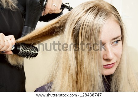 Hairdressers hands drying long blond hair with blow dryer and round brush