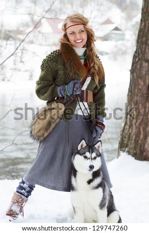 Happy young woman standing with siberian husky dog in winter forest