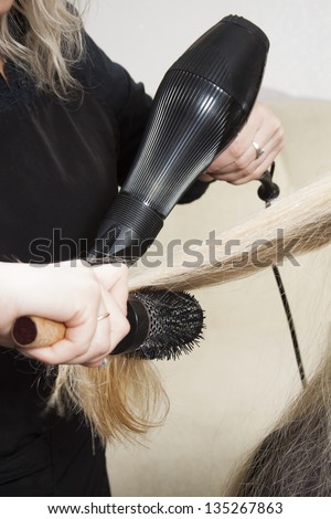 Hairdressers hands drying long blond hair with blow dryer and round brush