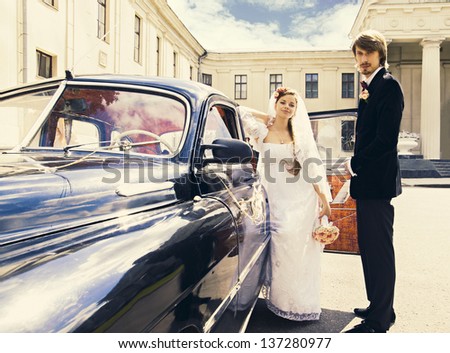 Beautiful happy young bride and groom standing near a retro auto
