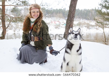 Happy young woman sitting with siberian husky dog in winter forest
