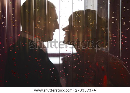 Romantic young wedding couple in love kissing in cafe. Candid view through window glass.