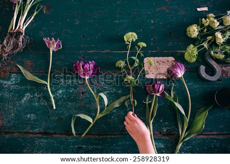 Florist workspace: woman making floral decorations; flowers on a old wooden table
