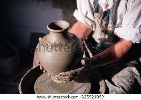 Craftsman holding a clay vase in his workshop; Potter holding ceramic vase.