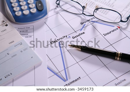 Calculator eyeglasses pen and check book on top of a graph showing expenses