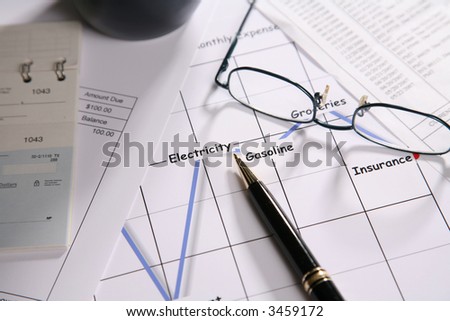 Coffee cup, eyeglasses, pen and check book on top of a graph showing expenses