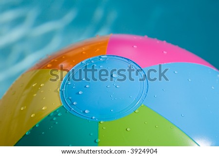 Close-up of beach ball with green, blue, pink,yellow and orange, water dropletts