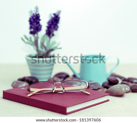 Eyeglasses on red diary and a watering can and vase of lavender.