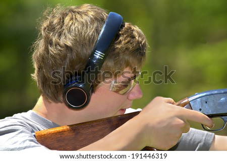 A young teenager learning to shoot targets with a shotgun.