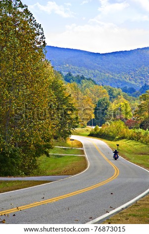 A motorcycle rider on a mountain highway surrounded by autumn colors.