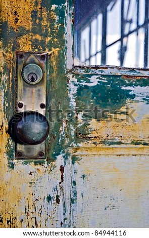 A old door knob in a metal door with peeling paint.