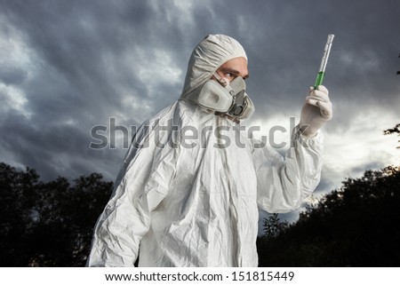 Scientist wearing a chemical protection suit takes a sample of contaminated water. On a background of nature.