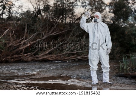 Scientist wearing a chemical protection suit takes a sample of contaminated water.  On a background of nature.
