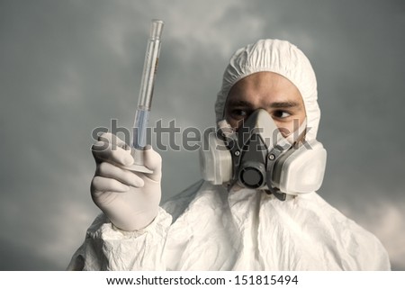 Scientist wearing a chemical protection suit takes a sample of contaminated water. On a background of sky.