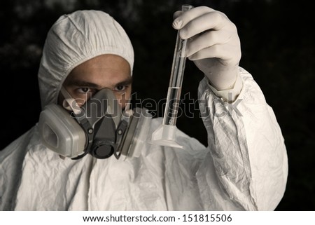 Scientist wearing a chemical protection suit takes a sample of contaminated water.  On a background of nature.