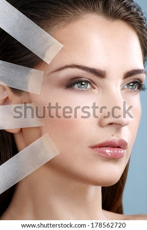 Beautiful woman applying tape lifting treatment on face on blue background