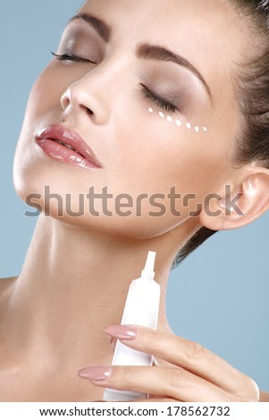 Beautiful woman applying cream treatment on her perfect face on blue
