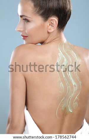 Beautiful woman applying scrub treatment on her back on blue