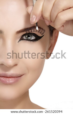 Model applying artificial eyelashes extension on smoky eye on white