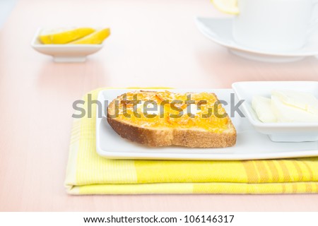 Breakfast. French toast with spread bitter orange marmalade or jam with candied peel, butter curls, lemon, a cup and dishware on wooden background