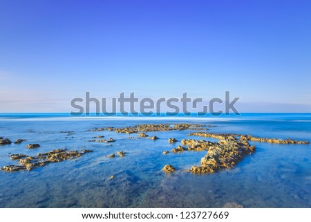 Rocks in a blue ocean under a clear sky on sunrise at morning. Tuscany, Italy. Long exposure photography