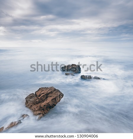 Rocks in a blue ocean waves under cloudy sky in a bad weather. Long exposure photography