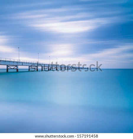 Industrial pier on the sea horizon. Side view. Long exposure photography in a cloudy day.