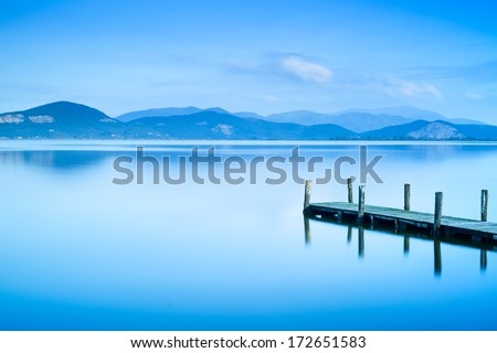 Wooden pier or jetty and on a blue lake sunset and cloudy sky reflection on water. Long exposure, Versilia Massaciuccoli Lake, Tuscany, Italy.