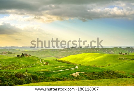 Tuscany, rural sunset landscape. Countryside farm, cypresses trees, green field, sun light and cloud. Volterra, Italy, Europe.