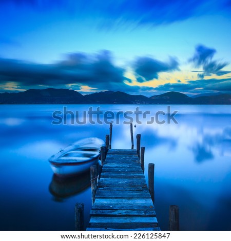 Wooden pier or jetty and a boat on lake sunset and sky reflection water. Long exposure, Versilia Massaciuccoli, Tuscany, Italy.