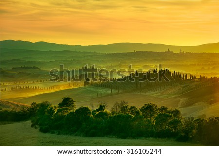 Tuscany, rolling hills on sunset. Crete Senesi rural landscape. Green fields, a farm with cypress trees and Siena city on background. Italy