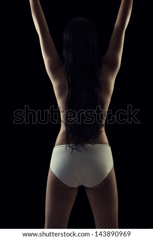 Back view of a indian modern nude girl raising up her arms against black