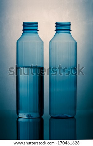 A water filled plastic bottle and an empty bottle on reflective surface