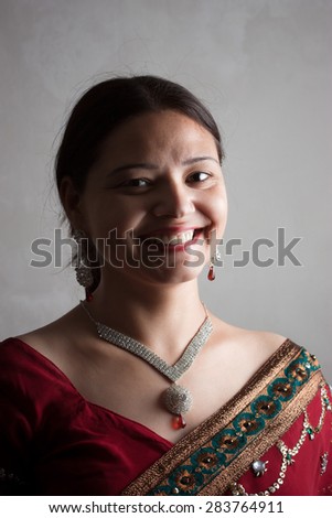 Portrait of a beautiful happy Indian woman wearing a designer red sari and attractive diamond jwellries over grey background