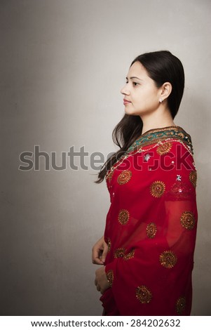 Portrait of a beautiful smiling Indian woman wearing a designer red sari over gray background