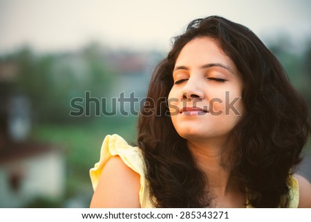 A beautiful Indian smiling girl feeling relaxed with closed eyes in the fresh air of the morning