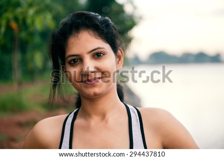 Happy indian girl relaxing after morning exercise very near to lake, looking at camera.