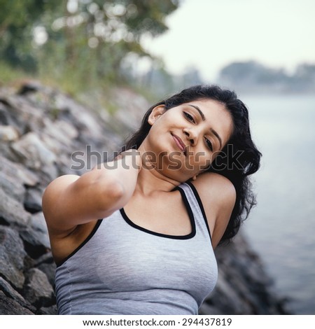 Happy indian girl sitting and relaxing after morning exercise very near to lake, looking at camera.