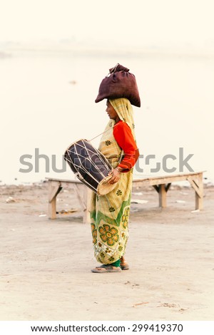 Varanasi, India - November 23, 2014: Indian villager woman in traditional dress sari walking and playing music at river side.