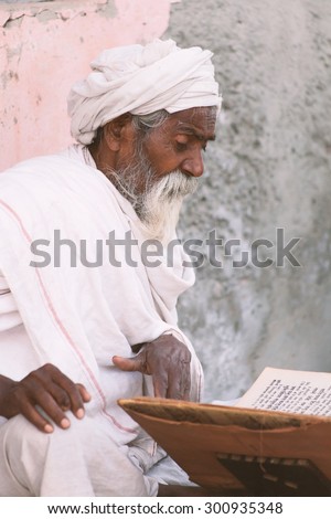 Close up of an old indian sadhu (saint) sitting and reading sacred texts near the temple.