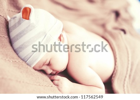 Sleeping sweet baby with cute hat on beige knit cover indoors
