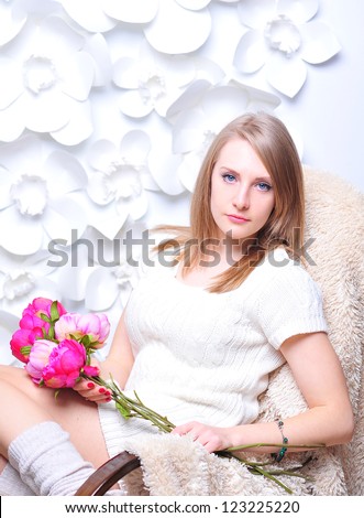 Young girl sitting in the rocking chair with white knitted dress and socks, holding pink flowers