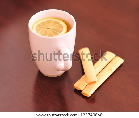White mug of tea with lemon on the brown table with cookies